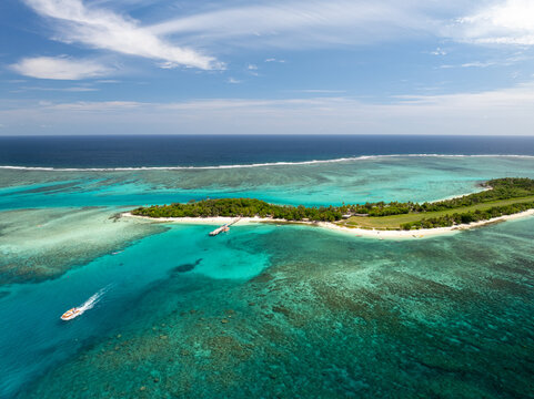 Aerial view of a long, thin island with lush green vegetation meeting the turquoise waters, as a boat cuts through the sea, Mystery Island, Vanuatu.
