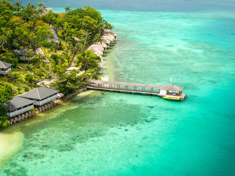 Aerial view of turquoise waters meet lush green shores lined with bungalows and a long pier reaching out into the sea, Port Vila, Shefa Province, Vanuatu.