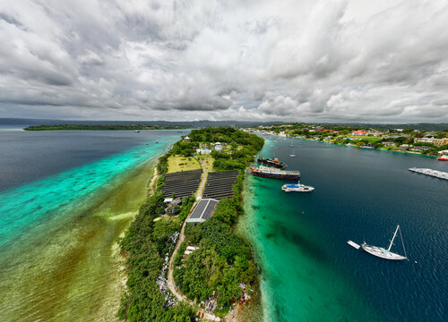 Aerial view of Iririki Island's lush green foliage meets the turquoise waters, framed by the city's edge and distant islands, Port Vila, Shefa Province, Vanuatu.