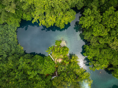 Aerial view of the Blue Hole framed by a vibrant canopy of green trees, creating a mesmerizing contrast of textures and tones, Espirito Santo, Vanuatu.