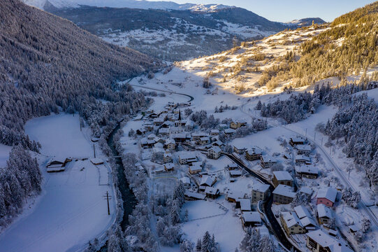 Aerial view of sun-kissed village nestled in a snow-dusted valley, where the river winds through the landscape of Andermatt, Uri, Switzerland.