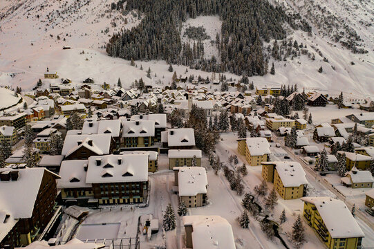 Aerial view of snow-laden rooftops and streets of a quaint village nestled against a backdrop of snow covered mountains, Andermatt, Uri, Switzerland.