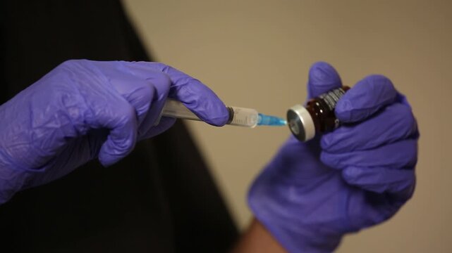 Close up of hands in medical gloves filling a syringe with vaccine from a vial. Doctor or nurse preparing for an injection procedure in a hospital or clinic.


