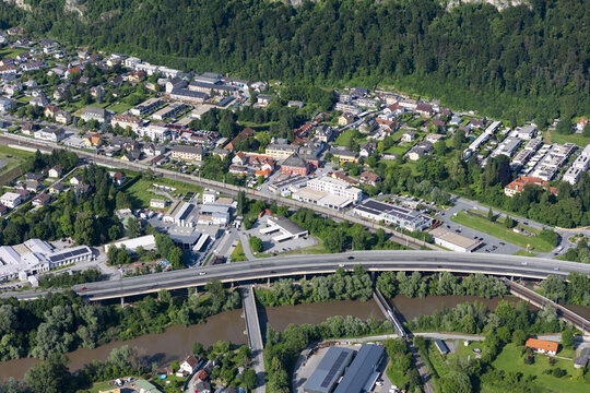 Aerial view of the Mur River flowing through the town, concrete bridges spanning its width, nestled against a backdrop of lush green forests, Peggau-Deutschfeistritz, Styria, Austria.