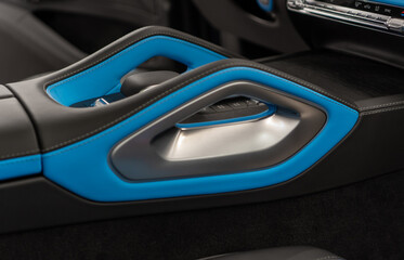 Fototapeta premium Black, blue leather interior details, steering wheel, badge, front seats, central console panel, shift knob, dashboard. Center console and cup holders, armrest between the front seats of a luxury car.
