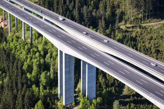 Aerial view of the towering bridge slicing through the verdant forest, cars speeding on the asphalt, contrasting with the lush green landscape, Wolfsberg, Carinthia, Austria.