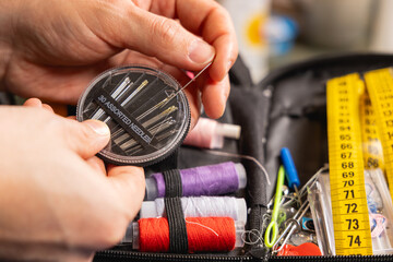 Une personne en train de choisir la taille d'une aiguille pour coudre. En arrière plan, une trousse à couture avec des bobines de fil. © Gautier Normand