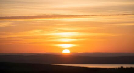 Fototapeta premium Vibrant orange and yellow sunset over a distant horizon with clouds and a body of water below