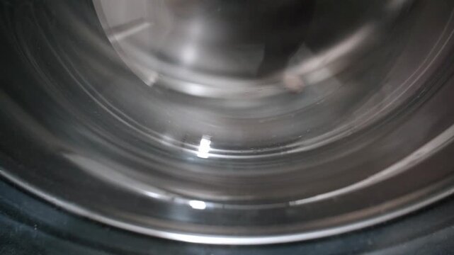 Detailed close up of a shiny stainless steel washing machine drum spinning rapidly during the laundry cycle, showing the metallic surface reflecting light and motion in a continuous loop