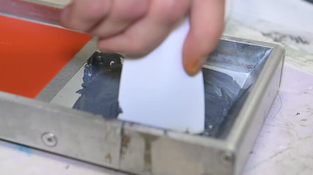 A man's hand mixes the ink in a silkscreen printing box in the workshop of a printing company