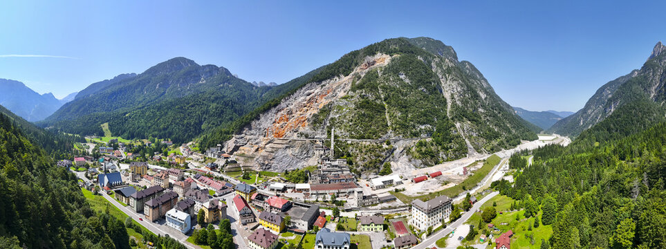 Aerial view of the village nestled amidst verdant mountains, revealing the stark contrast of the mine's bare rock face, Rabelj, Friuli-Venezia Giulia, Italy.