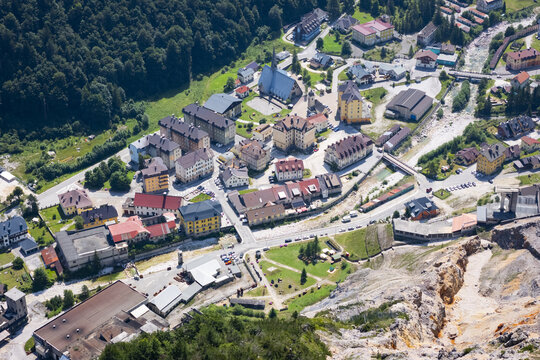 Aerial view of buildings nestled between lush green forests and rugged terrain, the river reflecting the sky above, creating a serene yet striking contrast, Rabelj, Friuli-Venezia Giulia, Italy.