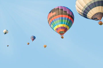 Fototapeta premium Vibrant rainbow-patterned hot air balloon leading a group across a bright blue sky.