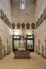 Bari, Italy. Side chapel inside the Basilica of San Nicola featuring a silver bust of St. Nicholas, sacred relics in display cases and historic ex-votos in a solemn setting.