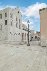 Bari, Italy. Side facade of the Basilica of San Nicola seen from Via Venezia in Bari, featuring Romanesque stone arches, historic architecture and an open square under a blue sky.