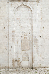 Bari, Italy. Ancient stone arched portal with carved tombstones and decorative inserts on a secondary facade of the Basilica of San Nicola in Bari, highlighting Romanesque sacred architecture.
