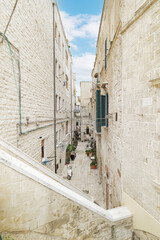 Bari, Italy. View of Vico X Corsioli from Via Venezia in Bari, a narrow historic alley framed by ancient stone buildings, balconies and plants, capturing daily life in the old town.