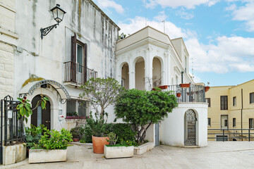 Bari, Italy. Facade of historic buildings and homes along Via Venezia in Bari, featuring stone architecture, balconies, plants and a quiet pedestrian atmosphere under a blue sky.