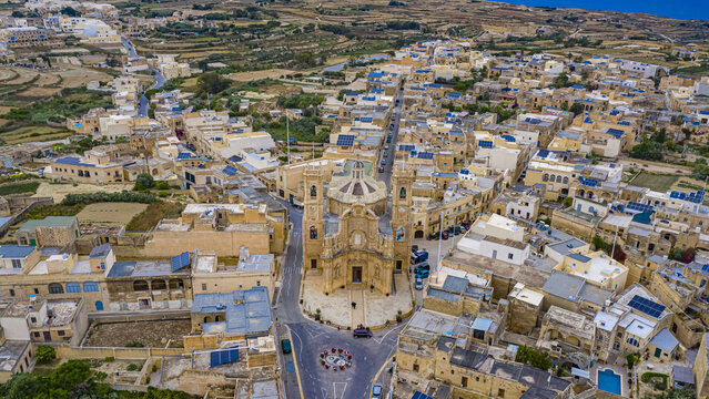 Aerial view of the majestic Basilica and Collegiate Parish church of the Visitation of Our Lady rises amidst a tapestry of golden stone buildings under the vast sky, Victoria, Malta.
