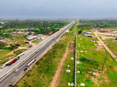 Aerial view of a long highway cutting through lush greenery and scattered buildings under an overcast sky, Okposi, Rivers, Nigeria.