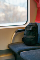 Black backpack standing on a train seat near a large window, representing travel preparation, commuting, movement, quiet moments in public transport