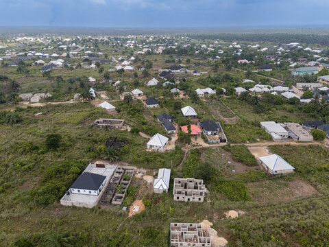 Aerial view of scattered buildings and uncompleted structures nestle amidst verdant fields under a vast sky, Oboh, Rivers, Nigeria.