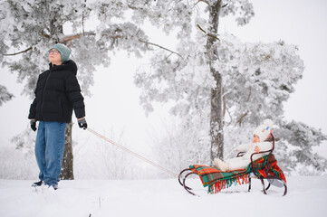 Boy pulling sled with baby in snowy winter forest