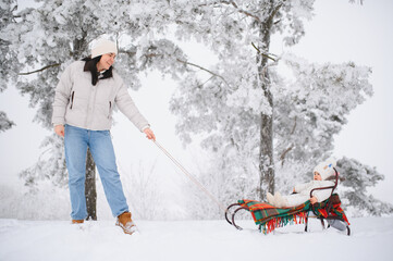 Mother sledding with baby in winter forest