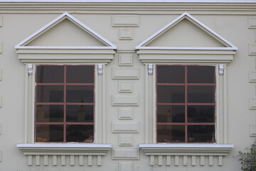 Symmetrical neoclassical windows with triangular pediments and decorative moldings on a cream building facade © Yeniceri