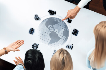 A diverse team engages in a strategy meeting, analyzing business data displayed on a virtual globe, surrounded by digital graphics and communication tools. Trope
