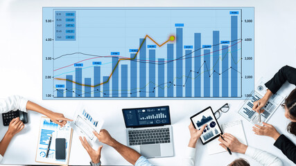 A diverse team collaborates in a modern office, analyzing business data on laptops and tablets, showcasing charts and graphs for strategic insights. Scalp