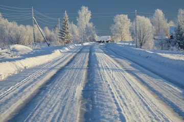 A winter road in a village with birch trees covered in frost and snow against a blue sky