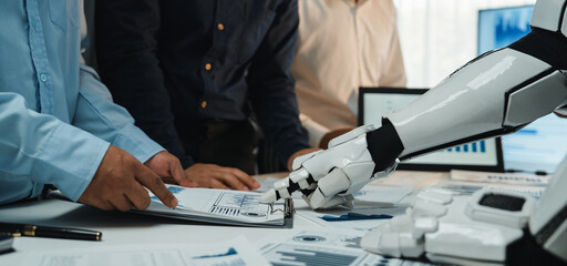 A modern office scene shows a robot arm assisting humans in data analysis, emphasizing teamwork and the integration of technology in professional environments.Noogenesis