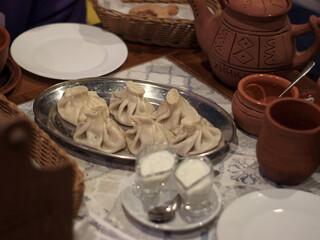 Traditional Georgian khinkali dumplings on metal platter with ceramic cups, matsoni and rustic tableware, cozy restaurant dining scene suitable for food menu, travel magazine, culinary article
