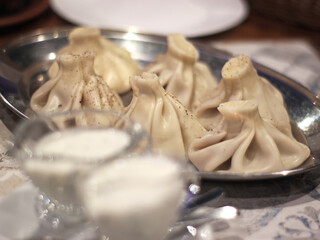 Close view of khinkali dumplings on metal platter with matsoni and black pepper, authentic restaurant food scene suitable for menu design, culinary article, food blog or travel publication.