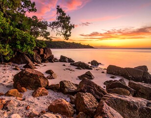 Seashore scene with boulders and sandy beach at sunset, colorful sky, and green trees in the top left corner