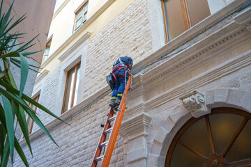 technician performing maintenance work on the cornice of a building using a ladder, Italy
