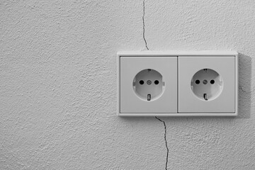 Double electrical wall socket mounted on a white textured wall with a visible crack. Minimalist...