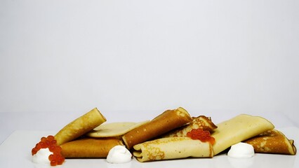 Rolled pancakes with red caviar and sour cream arranged on white background creating elegant appetizer food composition
