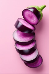 Whole purple eggplant sliced into even rounds, showcasing vibrant purple and white interior against a pink background, ideal for culinary and food-related themes