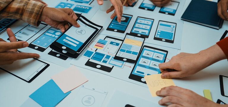 A dynamic workspace showcases hands engaged in a collaborative design process, creating mobile app prototypes and wireframes, reflecting teamwork and innovation in technology. SACTR