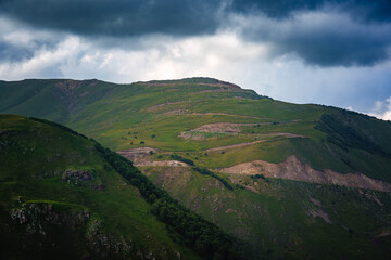 Green and rocky mountain slopes under dramatic cloudy sky. Mountain slopes with sunlight and shadows under dramatic clouds.No people. Perfect for nature and travel themes © Tommy