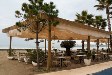 Coastal restaurant terrace with wooden tables, palm trees, and ocean view.
