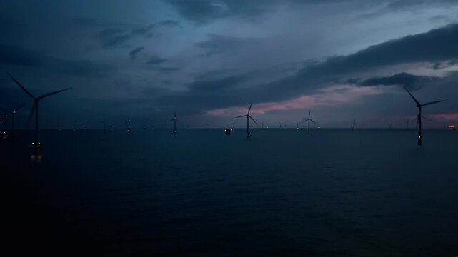 Lights flicker over turbulent waters, Distant silhouette of offshore windmills against stormy clouds