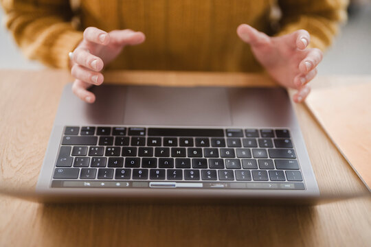 A person wearing a yellow sweater types on a laptop, their hands hovering over the keyboard.