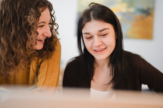 Two young women share a moment of laughter and engagement while looking at something together, fostering a sense of connection and shared experience.
