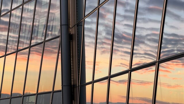 Close-up of modern skyscraper glass facade reflecting pink and orange sunset clouds