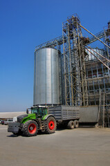 large tractor with cargo trailer near grain silos at elevator complex