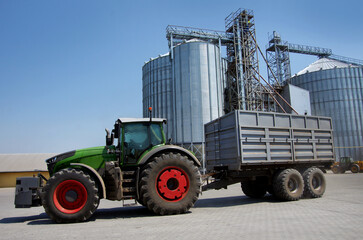 large tractor with cargo trailer near grain silos at elevator complex