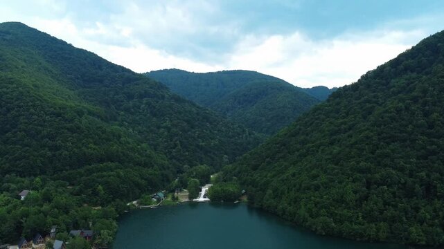 Aerial flight over lush green forested mountains risig from calm lake